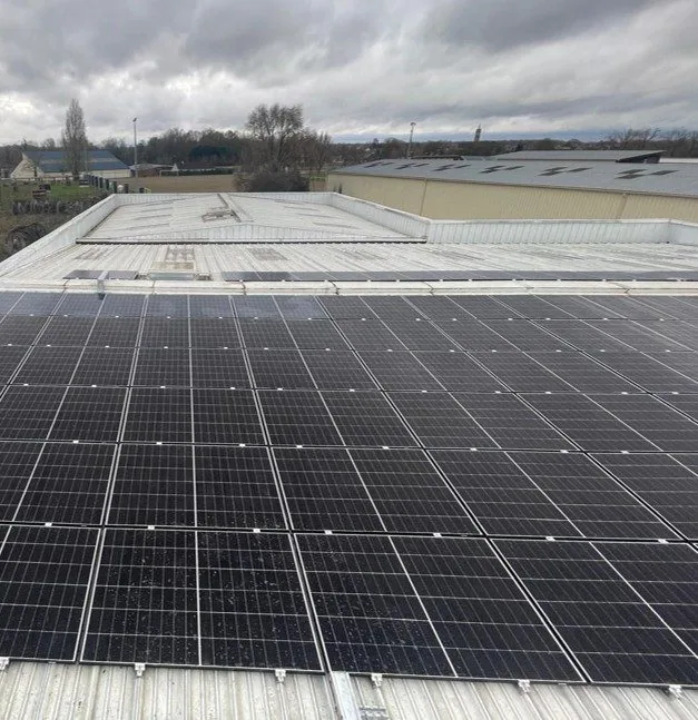 La centrale photovoltaïque d'Alésage XC vue vers l'horizon, panneaux au premier plan et bâtiments de la zone d'activité au fond